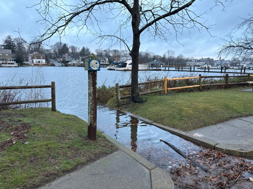 a sign on a sidewalk next to a body of water (MyCoast AI)