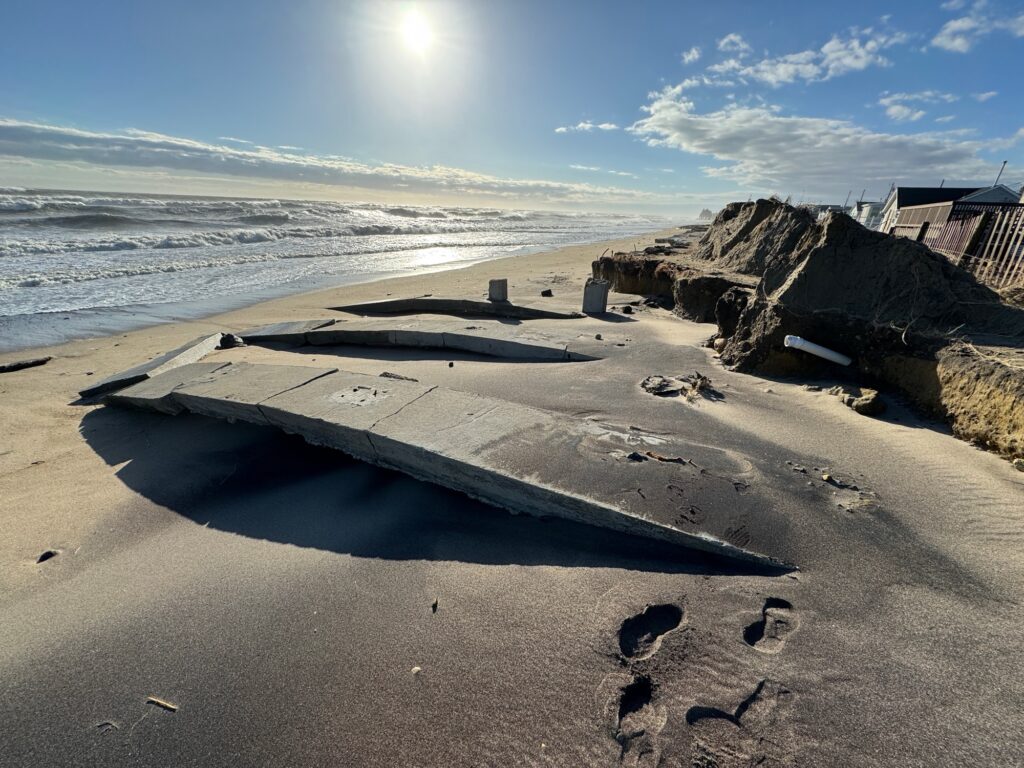a beach with a large hole in the sand and rocks and a building (MyCoast AI)