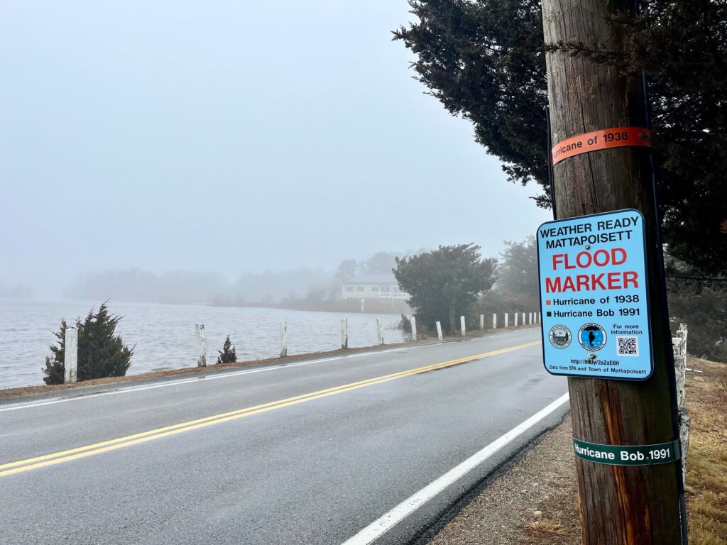 a sign on a pole by a road with water in the background (MyCoast AI)
