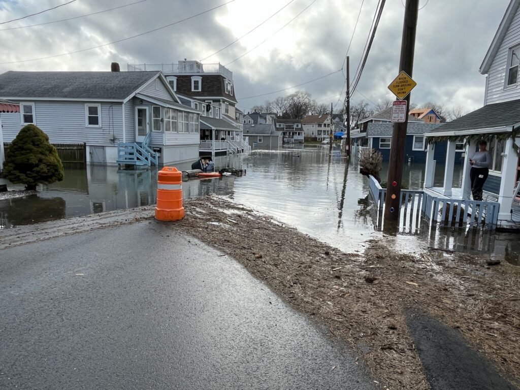 a flooded street with houses and a person standing on a boat (MyCoast AI)