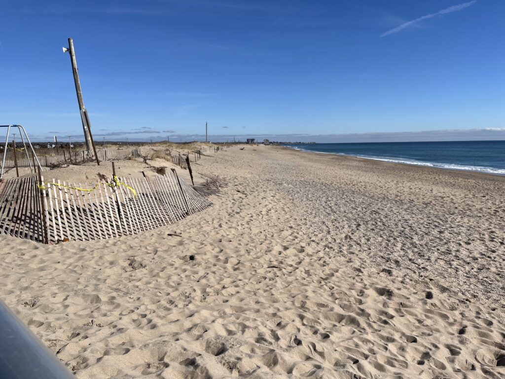 a sandy beach with a fence and a body of water in the background (MyCoast AI)