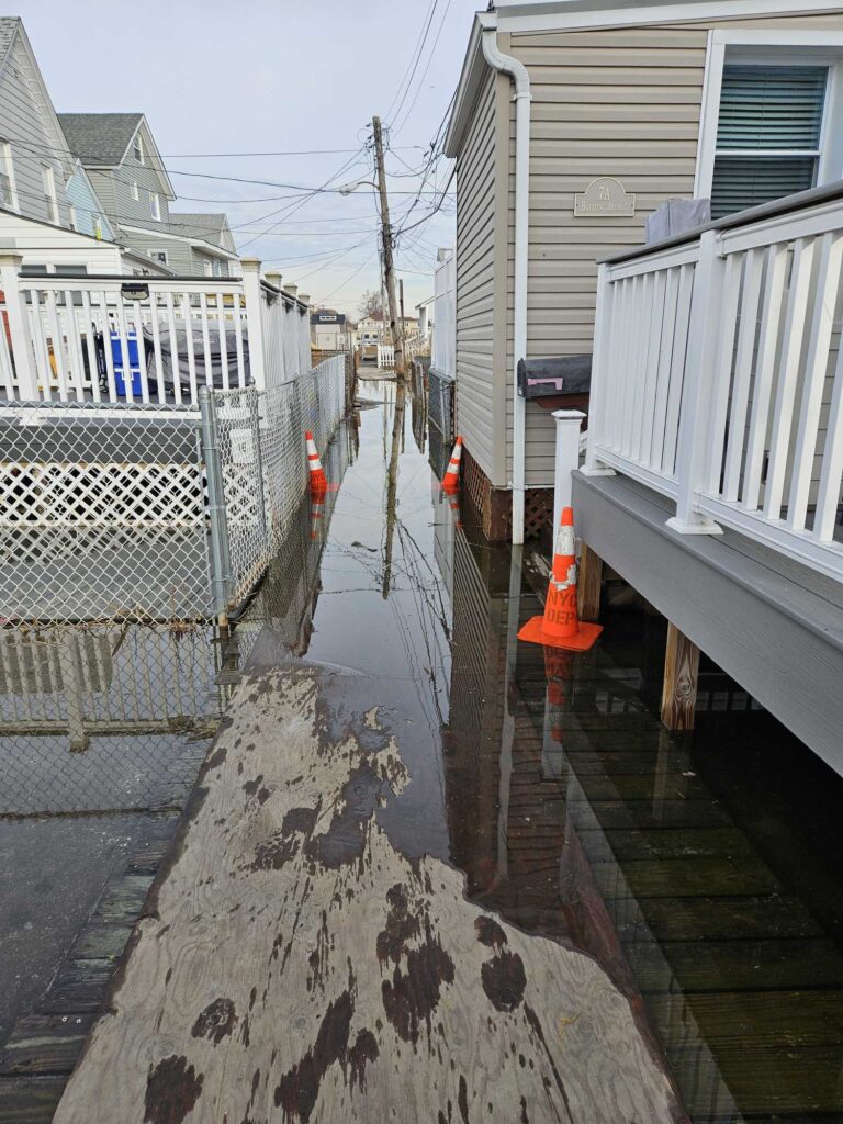 a wet street with a fence and buildings on the side (MyCoast AI)