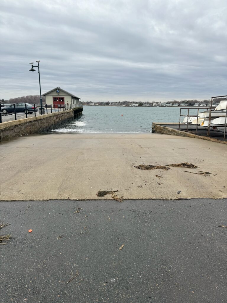 a sandy beach with a pier and a building with a body of water in the background (MyCoast AI)