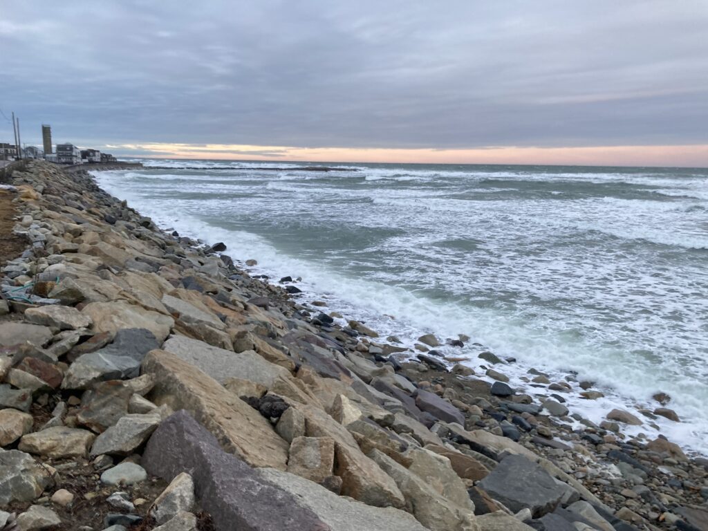 a rocky beach with a lighthouse in the distance (MyCoast AI)