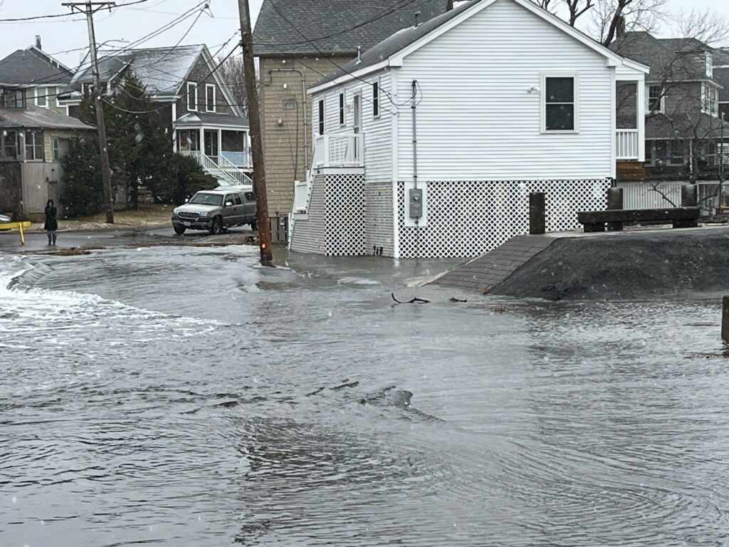 a flooded street with houses and a person walking on the sidewalk (MyCoast AI)