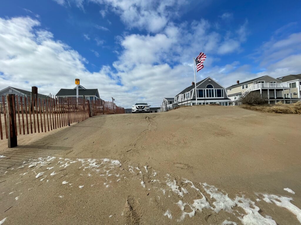 a sandy beach with a fence and a building with a flag on it (MyCoast AI)