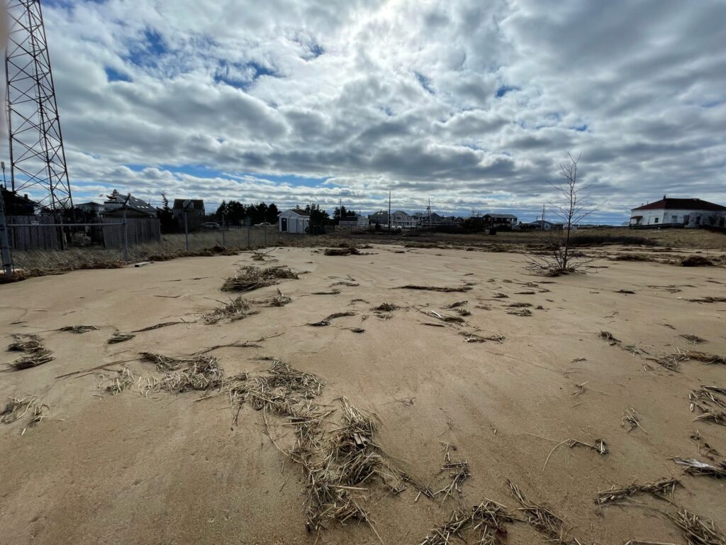 a sandy area with a fence and buildings in the background (MyCoast AI)