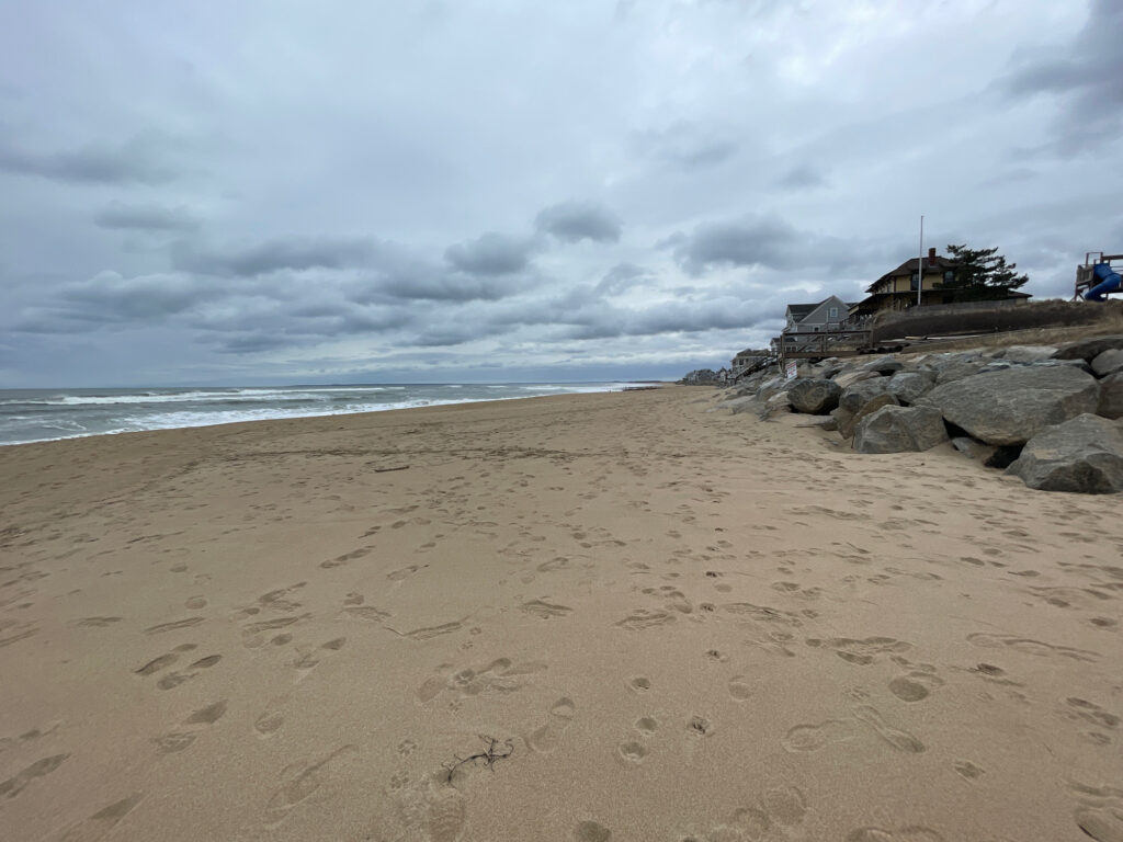 a sandy beach with rocks and a building in the distance (MyCoast AI)