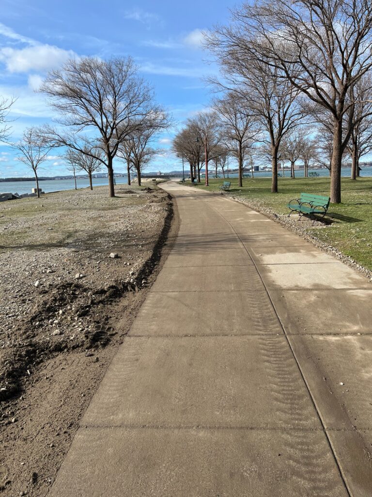 a sidewalk with benches and grass by a body of water (MyCoast AI)