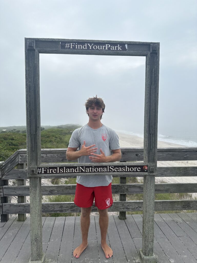 a man standing on a wooden deck with a sign on it (MyCoast AI)