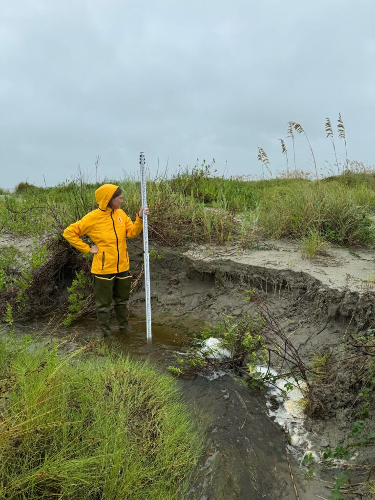 a person in a yellow jacket standing in a muddy area (MyCoast AI)
