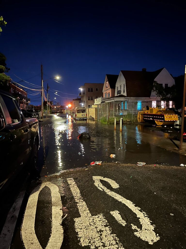 a street with a puddle of water on the side and buildings on the side (MyCoast AI)