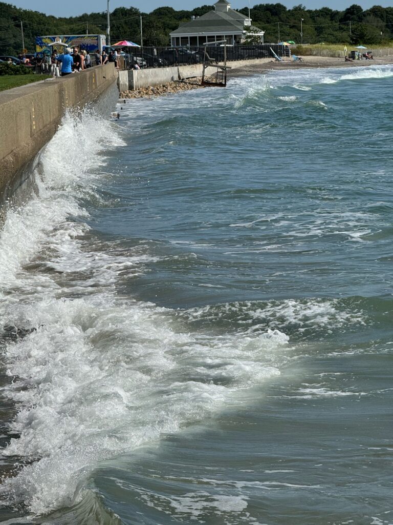 a body of water with waves crashing against a wall and people (MyCoast AI)