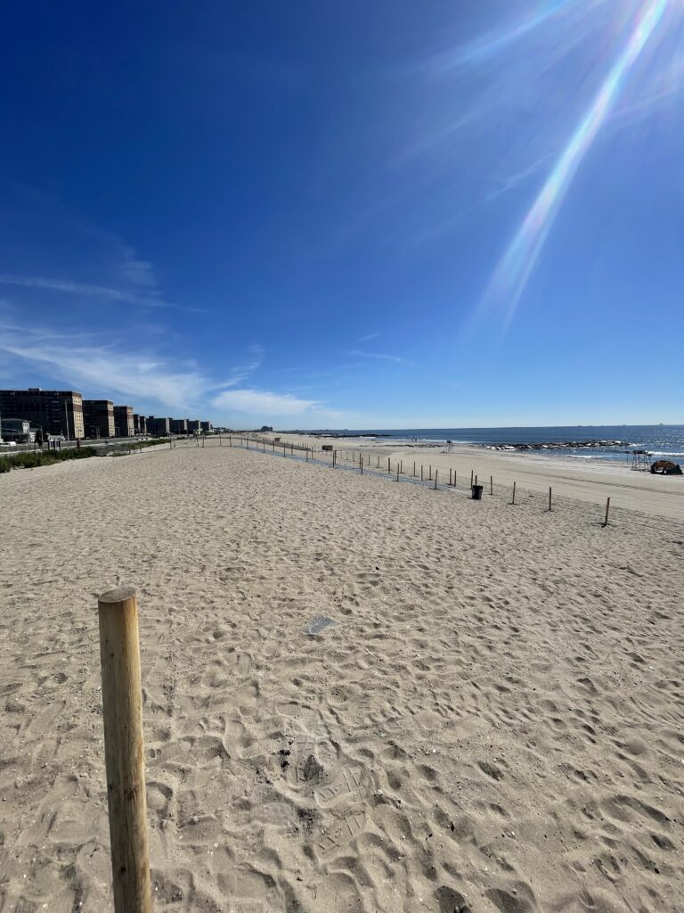 a sandy beach with a fence and buildings in the background (MyCoast AI)