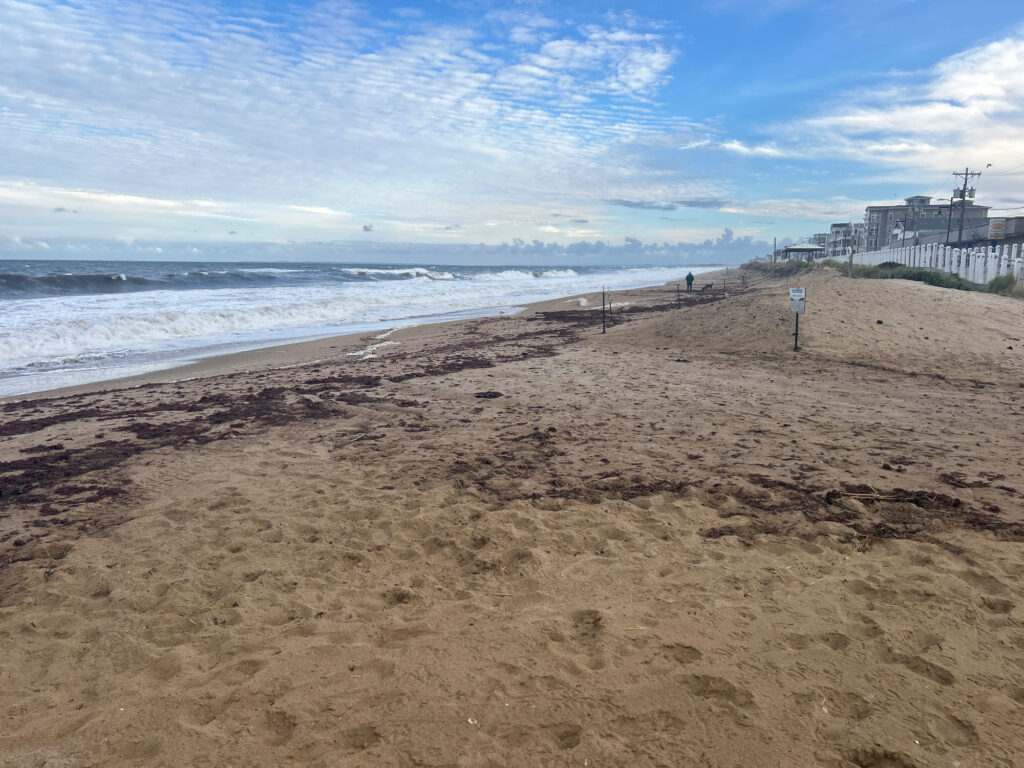 a sandy beach with a fence and buildings in the background (MyCoast AI)