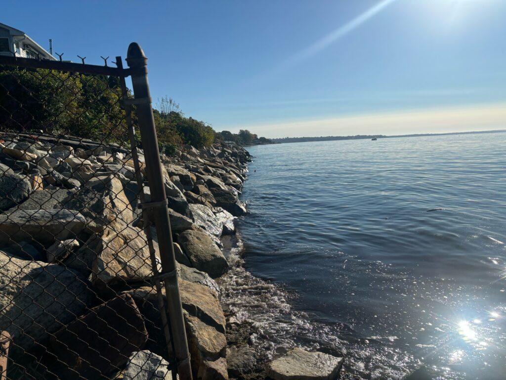 a rocky shore with a building and a body of water in the background (MyCoast AI)