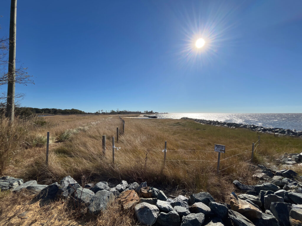 a rocky beach with a fence and a body of water in the background (MyCoast AI)