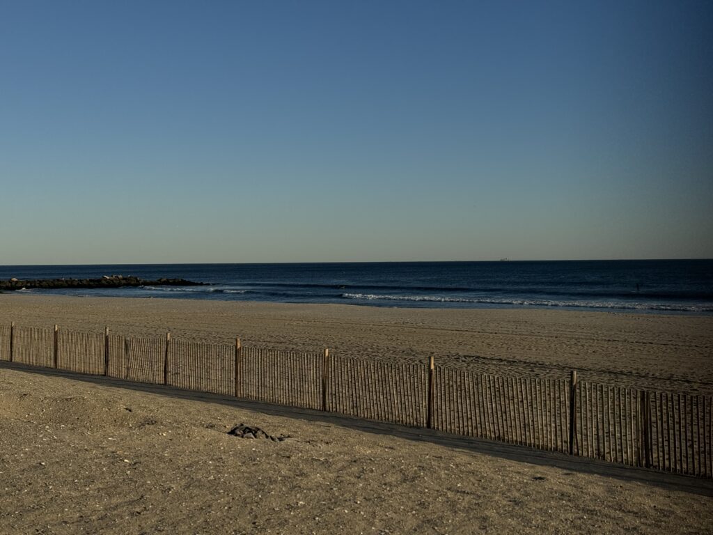 a sandy beach with a fence with Camber Sands in the background (MyCoast AI)