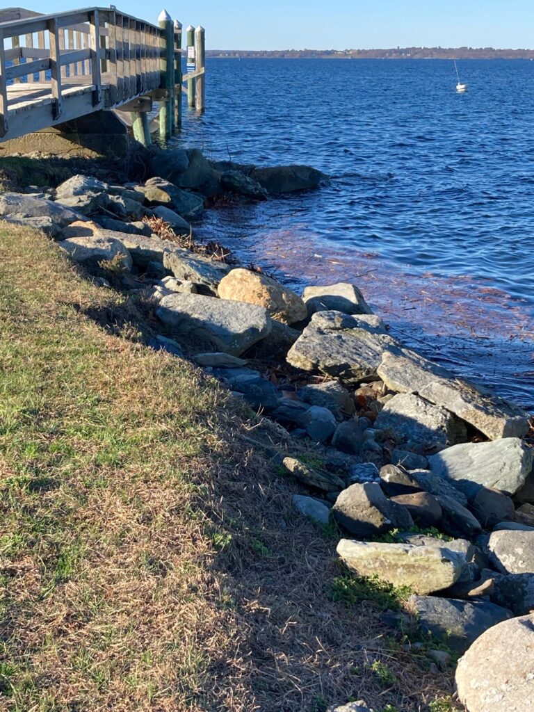a rocky shore with a dock and a boat in the distance (MyCoast AI)