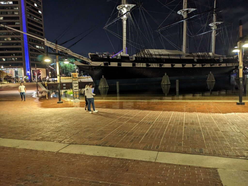 a couple of people walking on a brick walkway by a large ship (MyCoast AI)