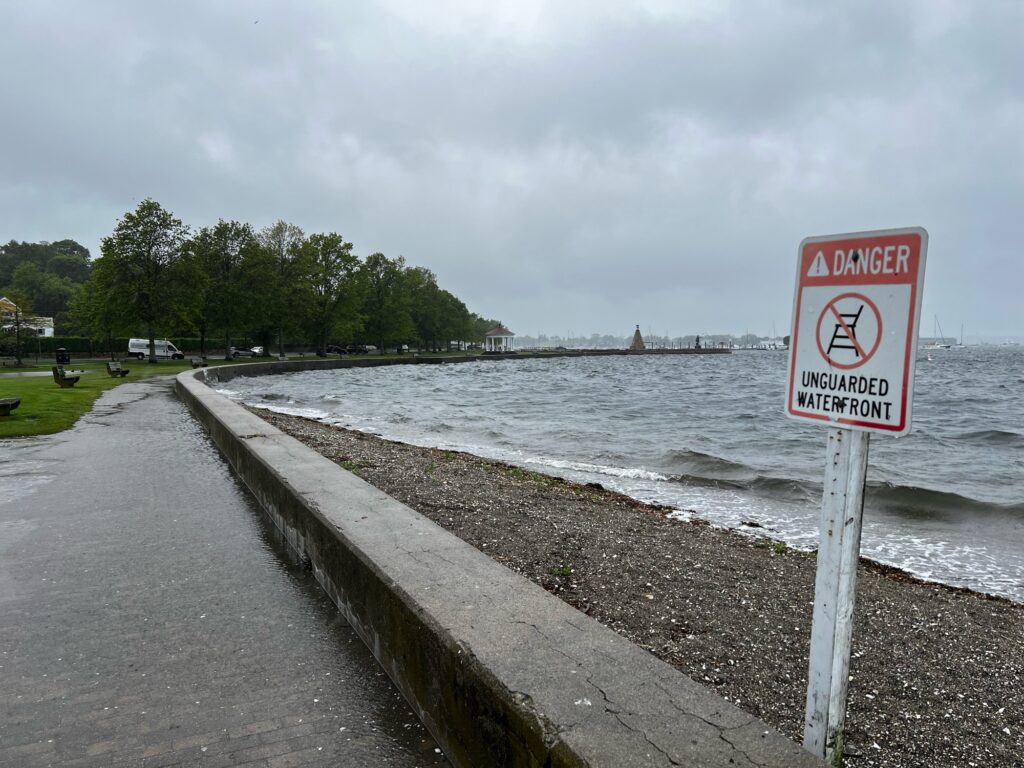 a sign on a sidewalk next to a body of water (MyCoast AI)