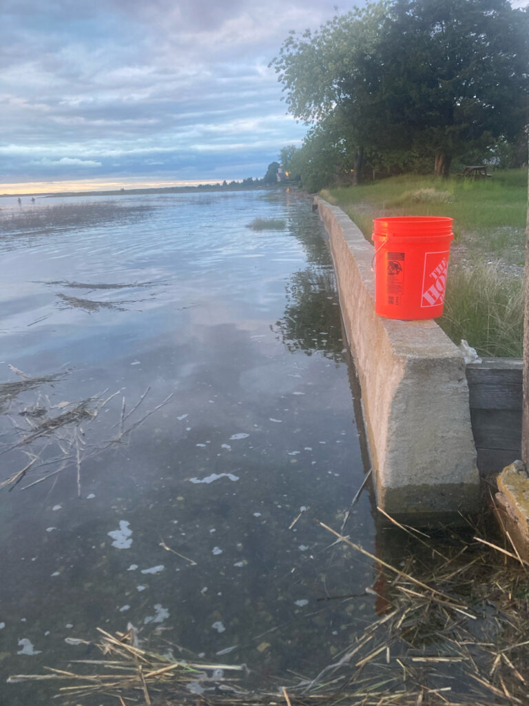 a red bucket on a concrete ledge by a body of water (MyCoast AI)