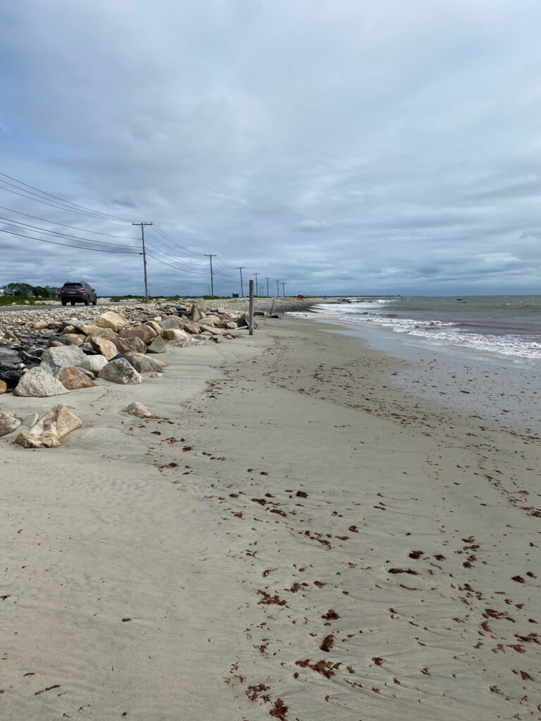 a sandy beach with rocks and a car parked on the side (MyCoast AI)