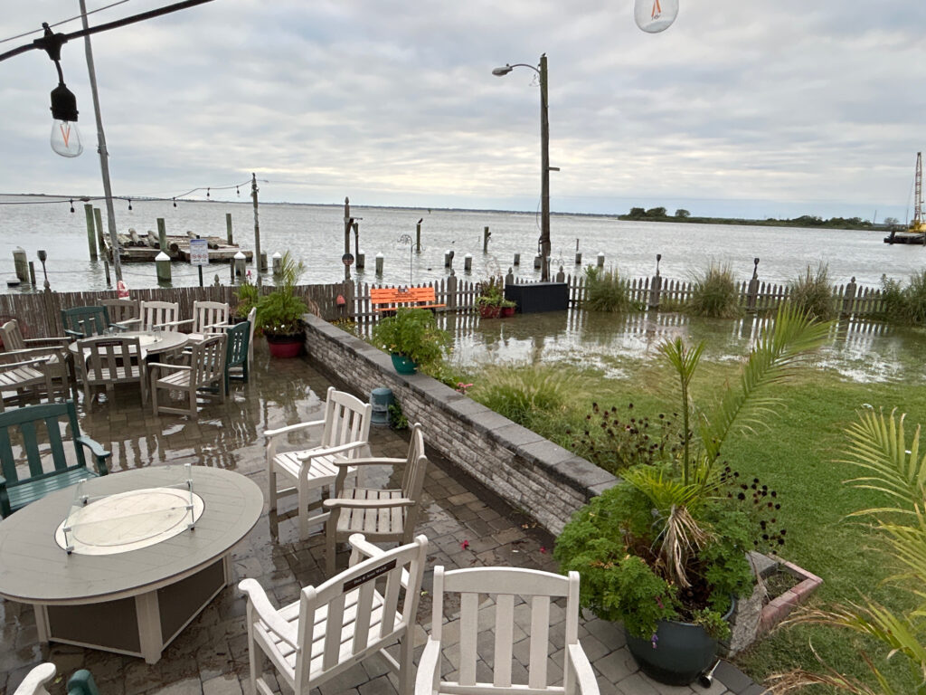 a patio with tables and chairs by a body of water (MyCoast AI)