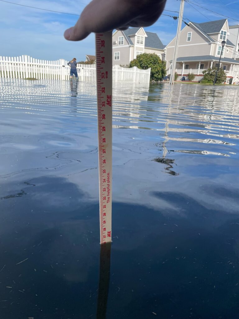 a hand holding a red measuring tape above water (MyCoast AI)