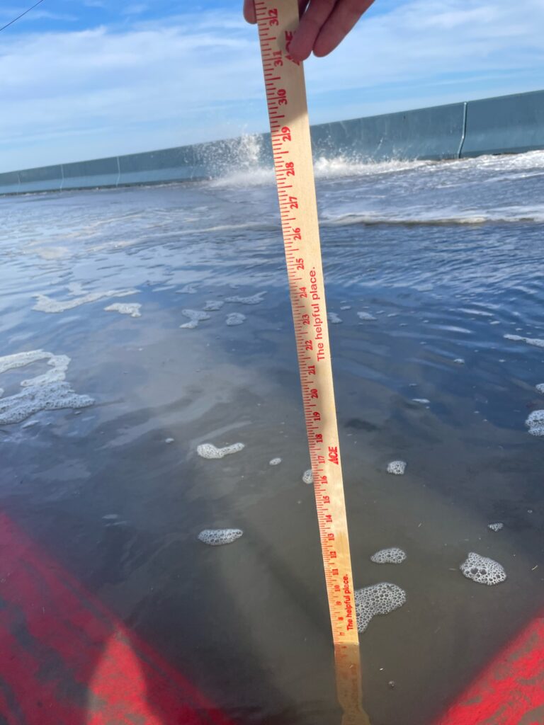a hand holding a red and white measuring tape above a body of water (MyCoast AI)