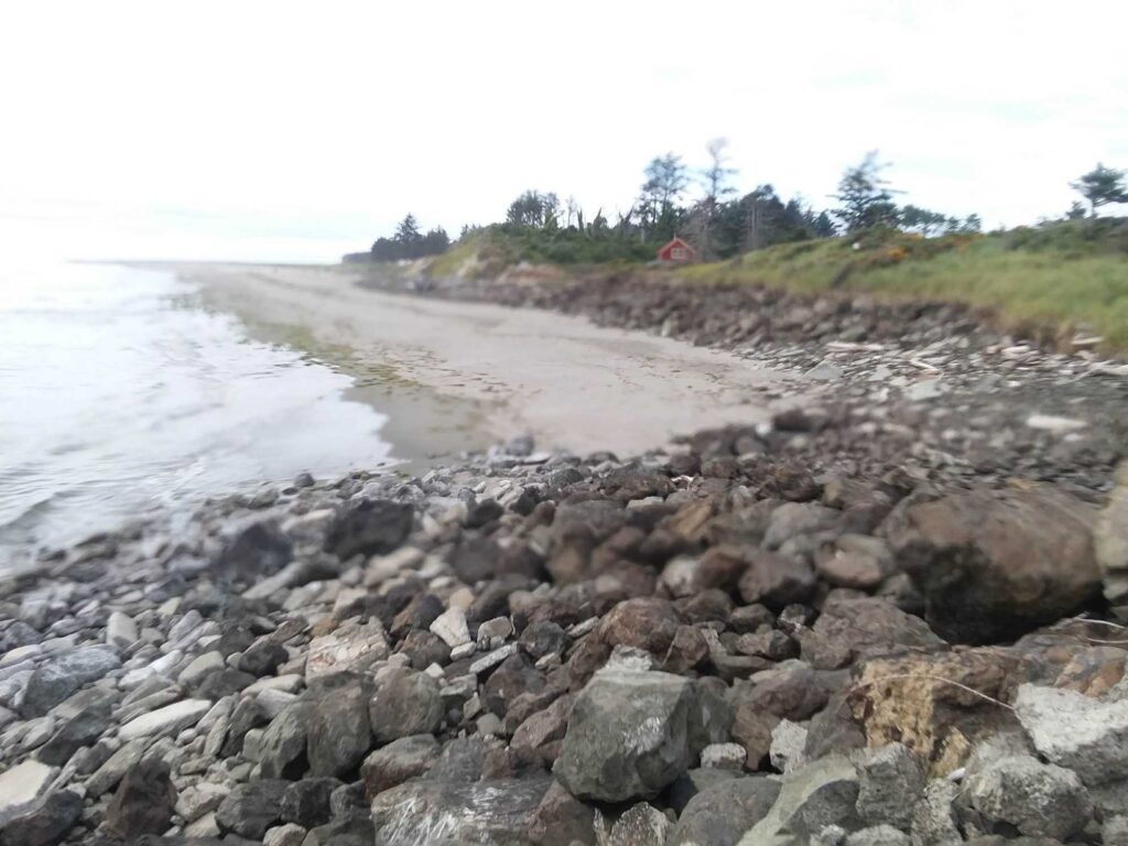 a rocky beach with a house in the background (MyCoast AI)