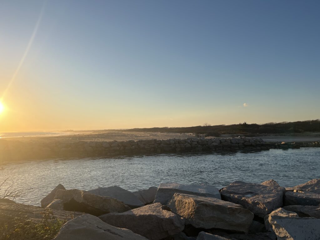 a body of water with rocks and a beach with the sun setting (MyCoast AI)